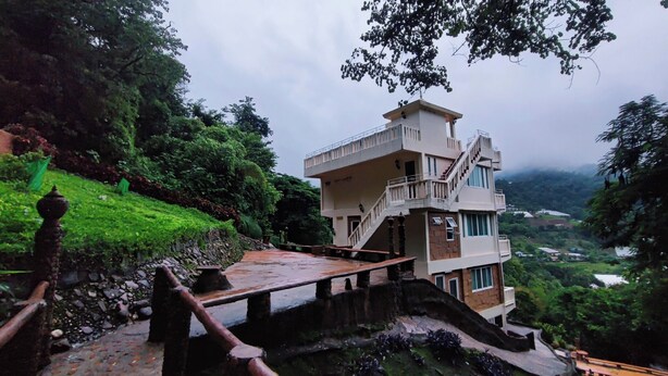 A multi-story building with a staircase leading to the upper levels, surrounded by lush greenery and a hilly landscape. - Baanpaya pano (Mae Rim)