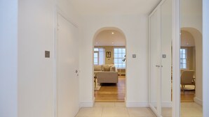Ein Flur mit weißen Wänden und Holzdielen, der zu einem Wohnbereich mit Sofa und Sessel führt.