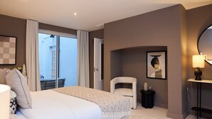 Ein modernes Schlafzimmer mit einem großen Bett, einem Sessel, einem kleinen Tisch und einem Balkon mit Vorhängen.