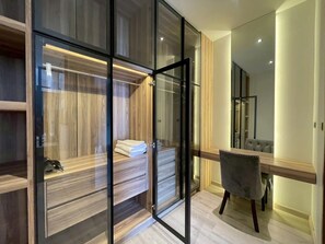 Un dormitorio moderno con un armario de vidrio, un tocador con espejo y una silla gris.