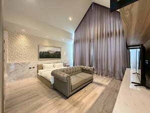 Un dormitorio moderno con pared de ladrillo, un ventanal con cortinas, una cama, un sofá y un televisor.