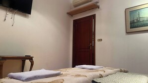 Ein Schlafzimmer mit einem Bett, einem Fernseher, einer Klimaanlage, einer Holztür und einem Bild an der Wand.