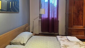 Ein Zimmer mit einem Bett, einem Holzschrank, einem Bild an der Wand und einem Fenster mit Vorhängen.