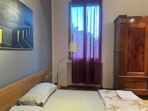 A room with a bed, a wooden wardrobe, a painting on the wall, and a window with curtains. - Room-b&b di Jerome Camera 1 (Bologna)