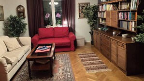 Un salon avec un canapé rouge, un canapé beige, une table basse en bois et une bibliothèque.