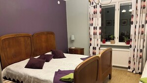 Une chambre à coucher avec un lit en bois, des oreillers violets, une couvre-lit blanche en dentelle et une fenêtre avec des rideaux.