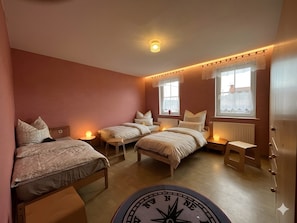 A bedroom with two beds, a wooden floor, a ceiling light, and a window with a view.
