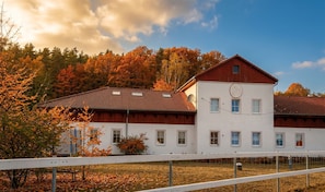 A two-story building with a red roof and white walls, surrounded by autumn foliage.
