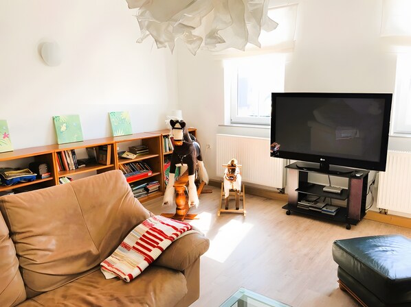 A living room with a sofa, a television, a bookshelf, and a window.