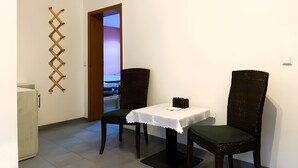 Una habitación con una mesa de comedor, dos sillas, un armario pequeño y una puerta que da a otra estancia.