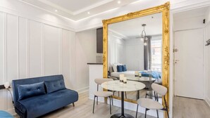 En moderne stue med en blå sofa, et rundt spisebord med stole og et stort spejl med gylden ramme.