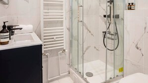 Et moderne badeværelse med en glasafskærmet brusekabine, en hvid vask og et toilet.