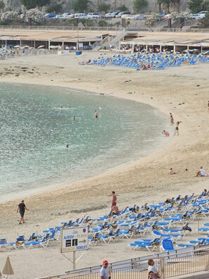 A beach with rows of blue and white sun loungers, a sign indicating amenities like showers and toilets, and a clear view of the sea. - Luxurious Apartment with Private Terrace and Garden in Las Palmas (Las Palmas)