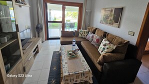 Un salón con un Galaxy S23 Ultra, un sofá con cojines estampados, una mesa de centro con un mantel individual y vistas al exterior a través de un ventanal.
