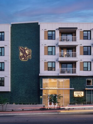 Un bâtiment moderne, avec un logo bien visible sur la façade, une entrée au niveau du sol et des balcons aux étages supérieurs.