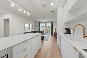 Une cuisine moderne avec des meubles blancs, un îlot central et une grande fenêtre.