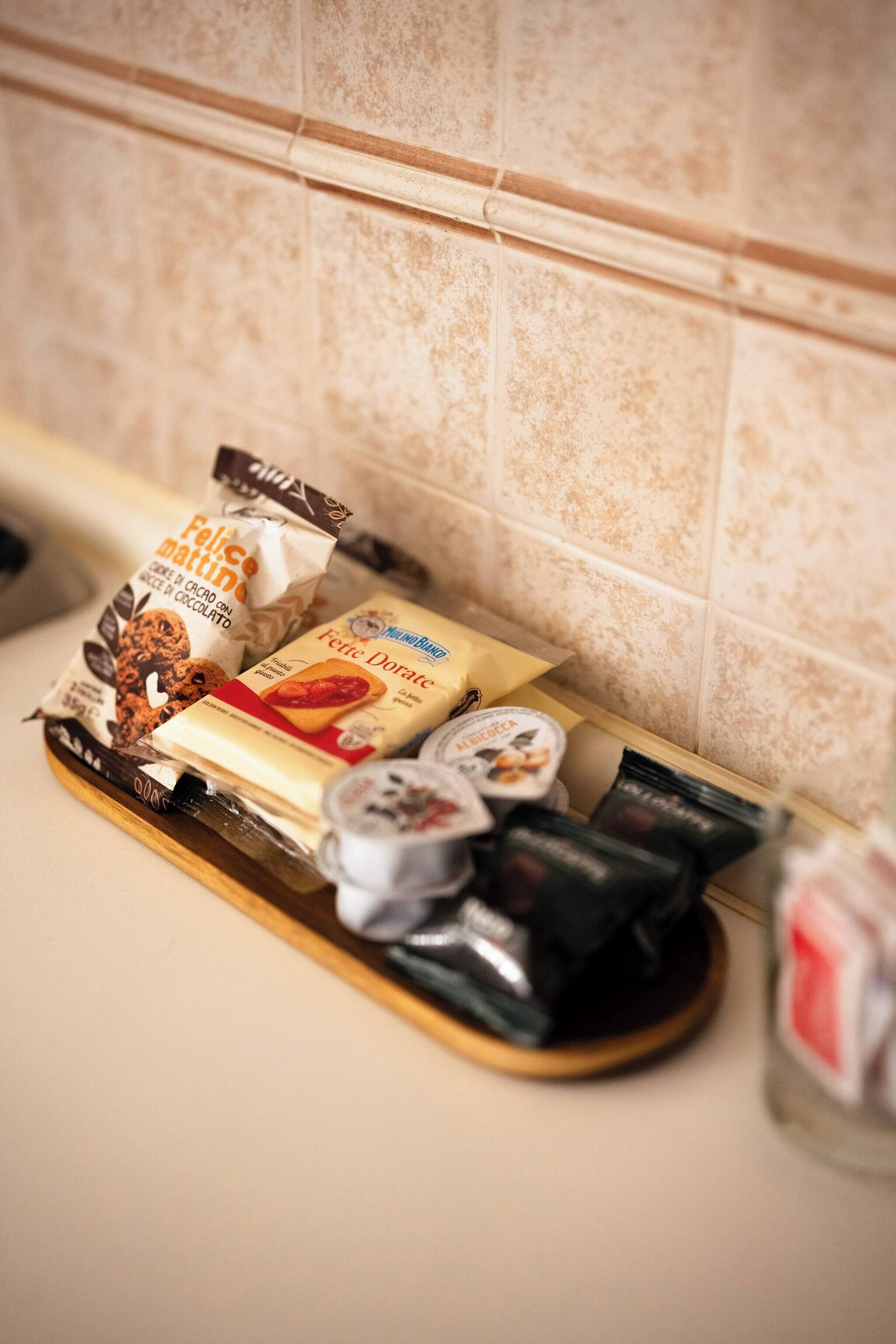 A kitchen counter with various food items and condiments, including a bag of cookies, a box of pasta, and several jars of spreads.