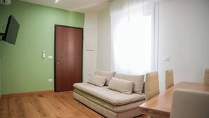 Quarto com parede verde, piso de madeira, sofá bege e mesa de madeira.