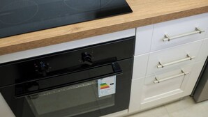 Uma cozinha com um fogão por indução preto, forno embutido e armários brancos.