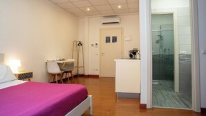Habitación de hotel con cama, escritorio, silla, kitchenette y zona de ducha.