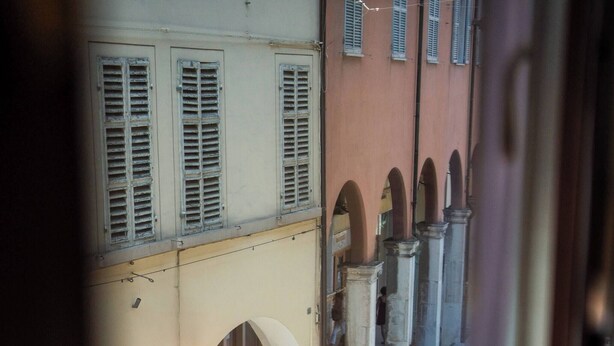 Una calle estrecha con un puente, pilares de piedra y un edificio con contraventanas.