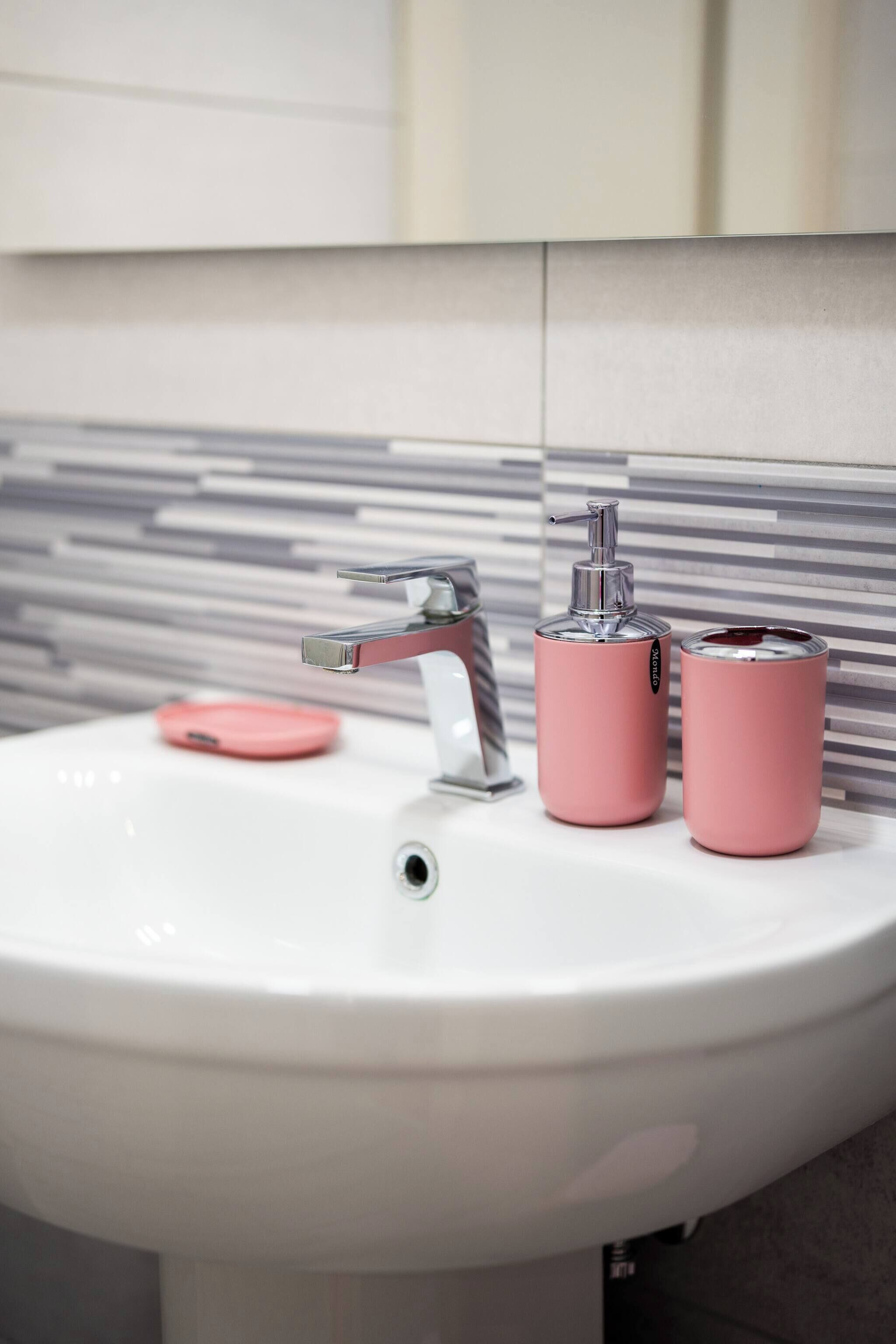 A bathroom sink with a modern faucet, a pink soap dispenser, and a pink soap dish.