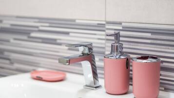 A bathroom sink with a modern faucet, a pink soap dispenser, and a pink soap dish.