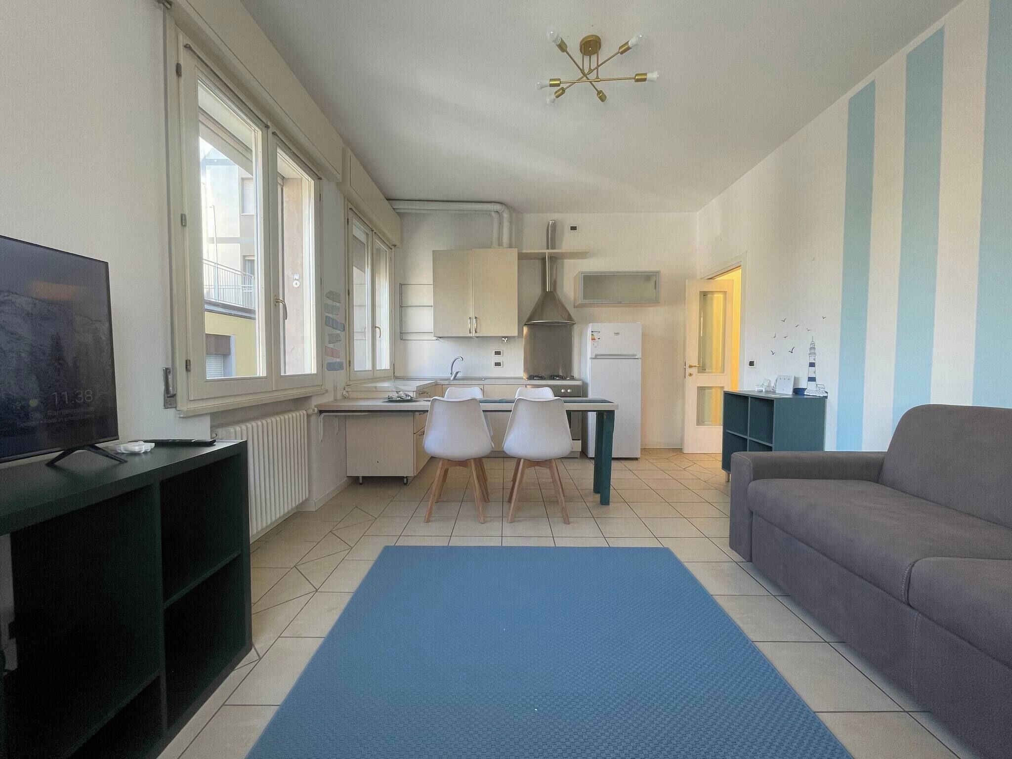Ett kompakt bostadsutrymme med ett litet kök, en matplats med stolar, en soffa och en tv som står på ett TV-bord.
