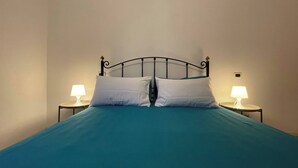 A single bed with a teal bedspread and white pillows, flanked by two bedside lamps on matching nightstands. - Charming Canal-side Apartment in Cesenatico, Italy (Cesenatico)