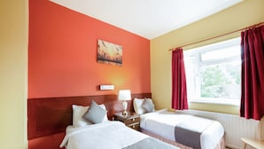 A hotel room with two beds, a window with red curtains, a painting on the wall, and a bedside table with a lamp. - Standard Twin Room (Gateshead)