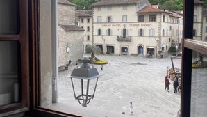 Blick aus einem Fenster auf einen Innenhof mit dem Grand Hotel Termé Roseo, Steinbauten und einem bewaldeten Hügel.