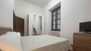 Ein Schlafzimmer mit Bett, Kommode, Fernseher, Fenster und Heizkörper.