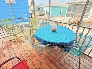 Un espacio al aire libre cubierto con una mesa redonda y sillas, un cuenco de vidrio sobre la mesa, y una vista de casas al fondo.