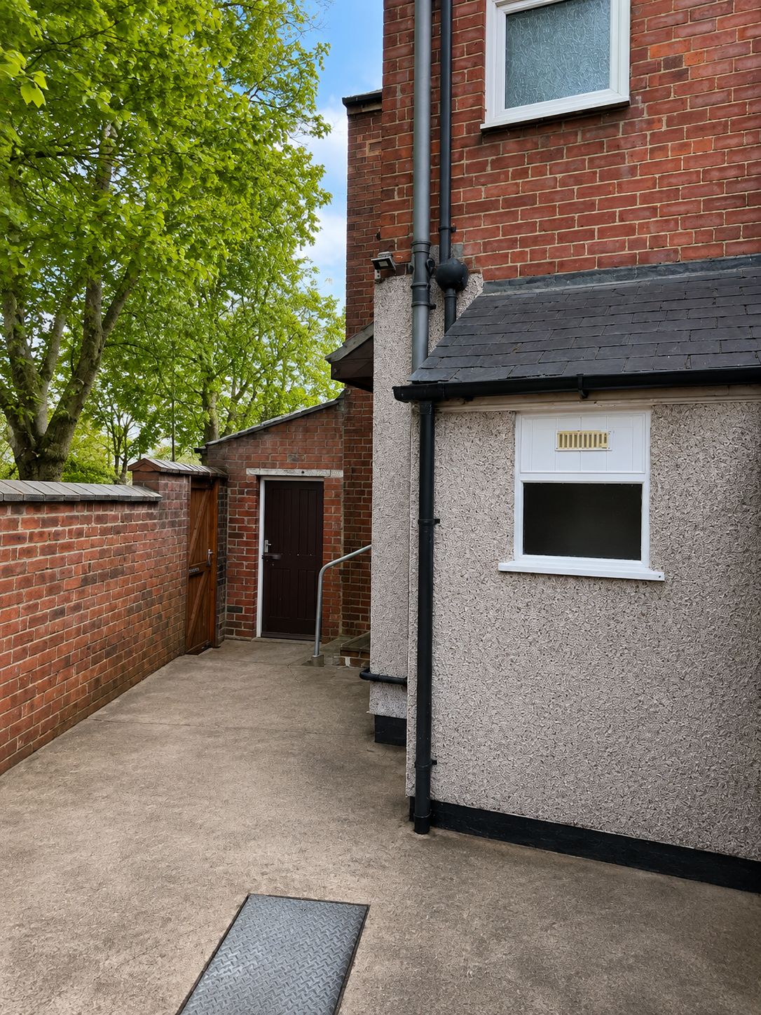 A narrow pathway leading to a building with a small window and a door.
