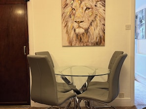 A dining area with a glass table and two grey chairs, a wooden door, and a lion painting on the wall. - Home for 9 | Contractors or Families | Free Parking |Near Doncaster Centre & M18 (Doncaster)