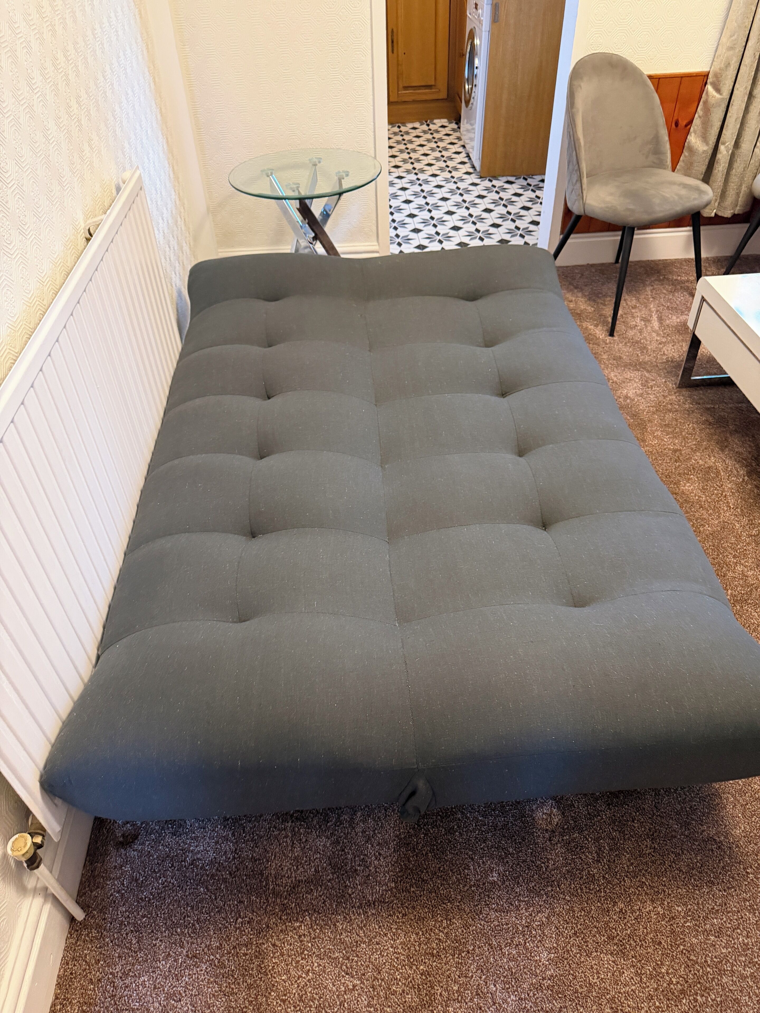 Une pièce comprenant un canapé capitonné, une table en verre, une chaise et un sol à motifs.