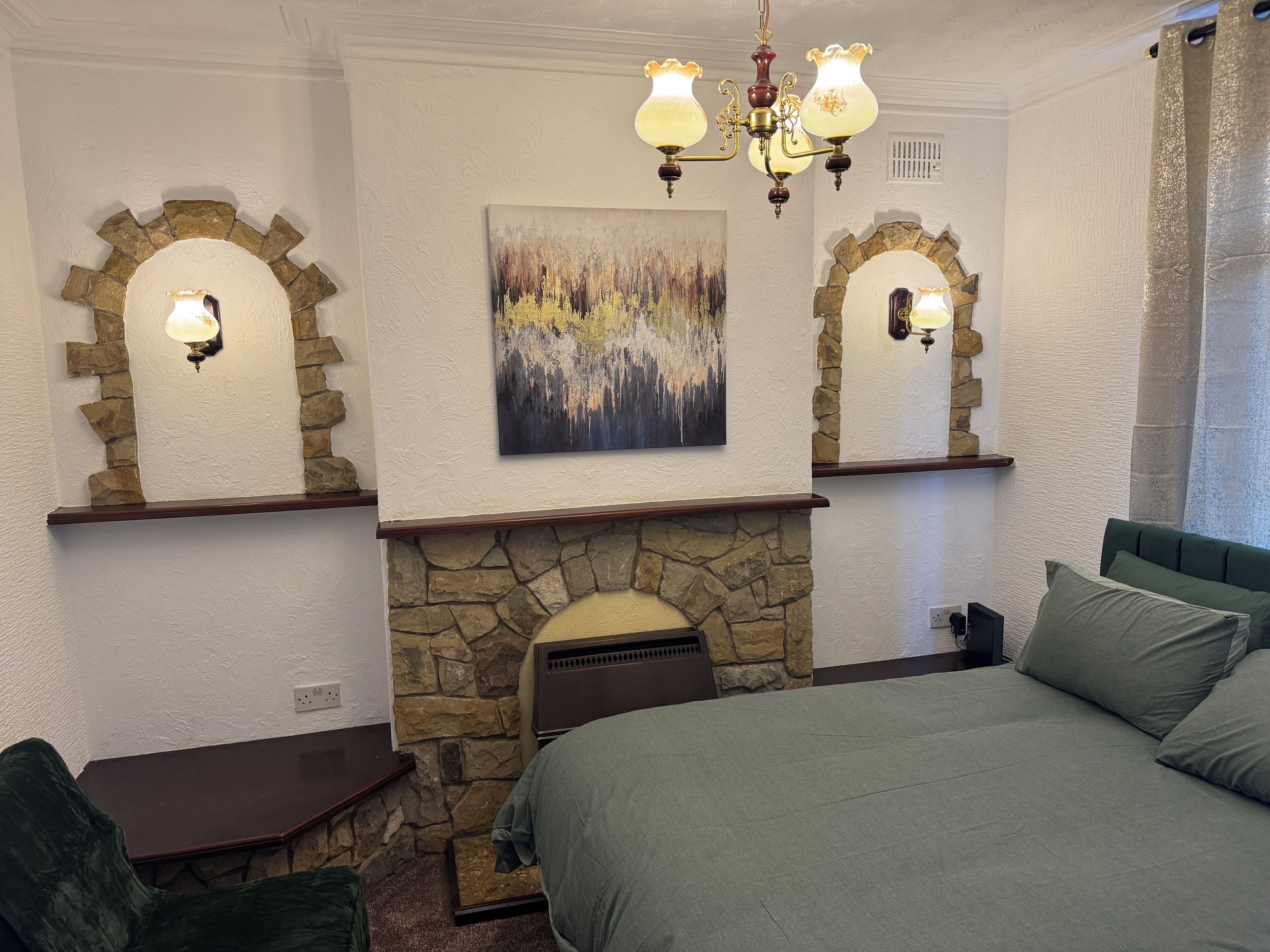 Un dormitorio con chimenea de piedra, una cama, un escritorio y dos apliques de pared.