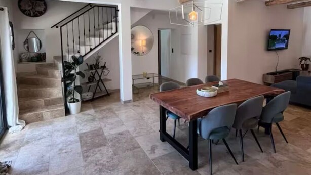 Amplia sala de estar con una mesa de comedor de madera, sillas grises y una escalera que lleva a otro nivel.