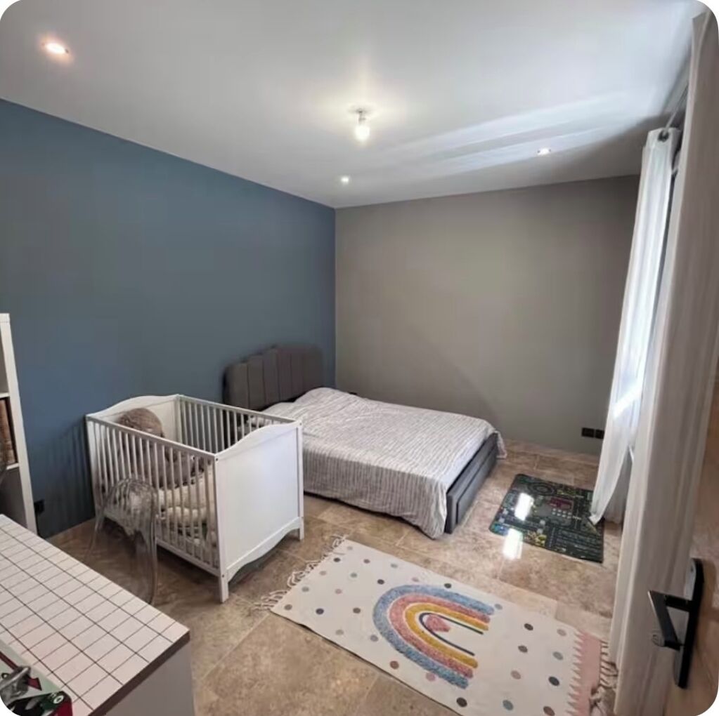 A room with a crib, a bed, a small rug, and a radiator.
