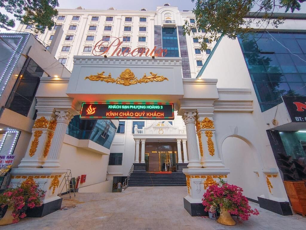 The entrance of a hotel with a large sign reading "Phoenix" and a digital display above the entrance.