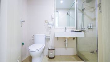 A bathroom with a toilet, a sink, a mirror, and a shower enclosure.