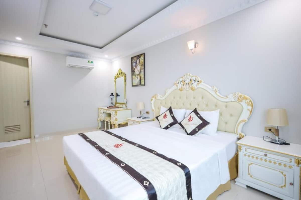 A hotel room with a large bed, a bedside table with a lamp, a wardrobe, and an air conditioning unit on the wall.