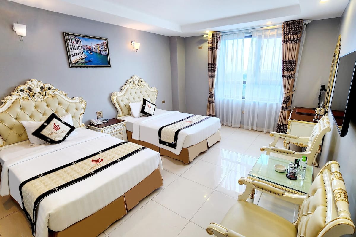 A hotel room with two beds, a television, a glass table, and a painting on the wall.