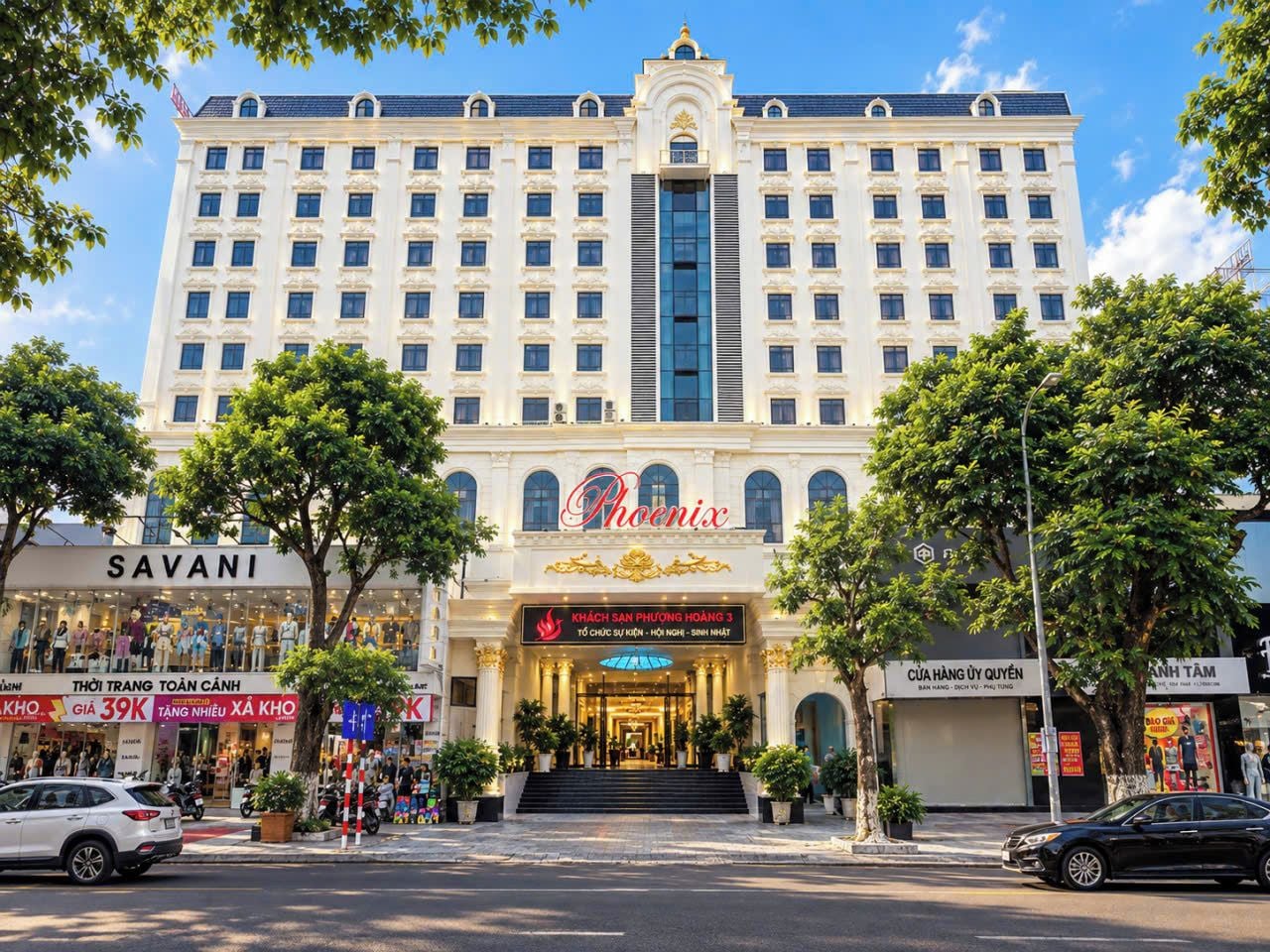 A multi-story hotel with a prominent entrance, a large sign reading 'Phoenix,' and several storefronts on the ground level.