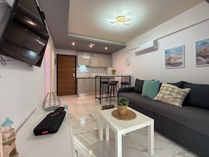 A modern living room with a grey sofa, a white coffee table, and a TV mounted on the wall. - Welcome to ILEKTRA Suite no.4 By SDR (Paralia)
