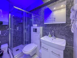 Et moderne badeværelse med en brusekabine med glasdøre, et hvidt toilet og en vask med et spejl over.