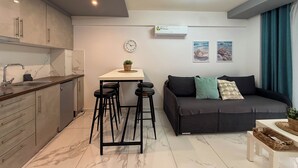 Eine moderne Küche mit Marmorarbeitsplatte, einer Essecke mit Hockern, einer Couch mit Kissen und einer wandmontierten Klimaanlage.
