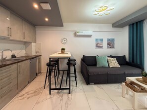 A modern kitchen with a marble countertop, a dining area with stools, a sofa with cushions, and a wall-mounted air conditioner. - Welcome to ILEKTRA Suite no.4 By SDR (Paralia)