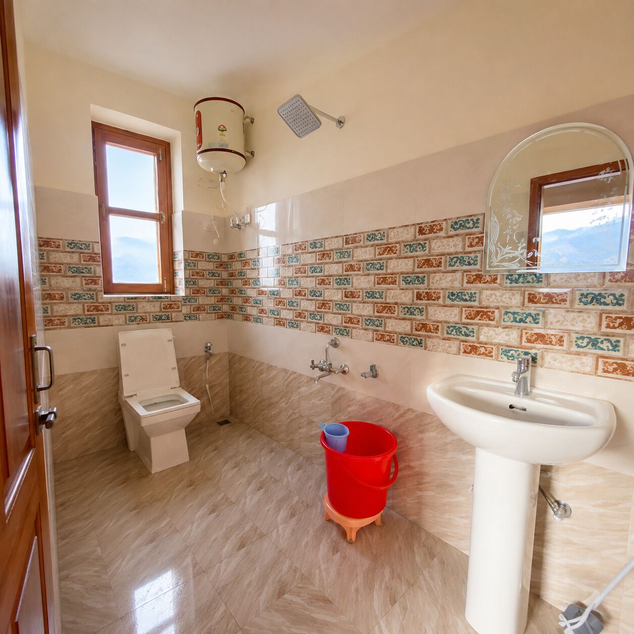 A bathroom with a toilet, sink, shower, and a red bucket on the floor.