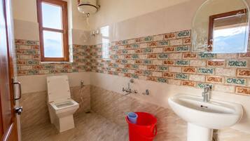A bathroom with a toilet, sink, shower, and a red bucket on the floor.